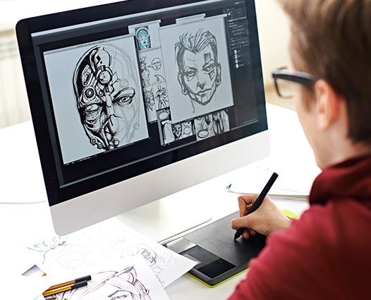 Student working on digital artwork with a stylus and drawing tablet, creating character designs displayed on a computer monitor.