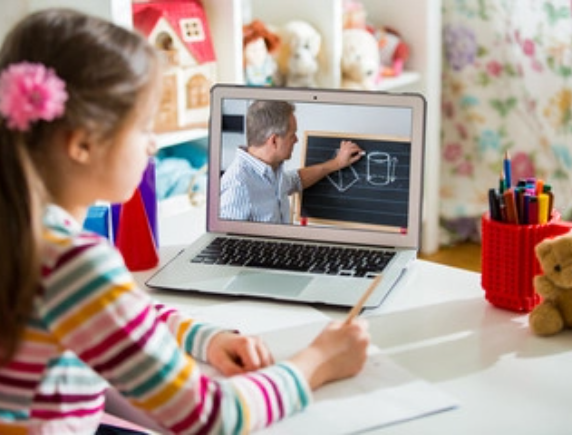 Young girl with a flower clip in her hair attending an online lesson on her laptop, watching her teacher draw geometric shapes on a chalkboard. This image represents the flexible and engaging virtual learning experience for FLVS elementary students.
