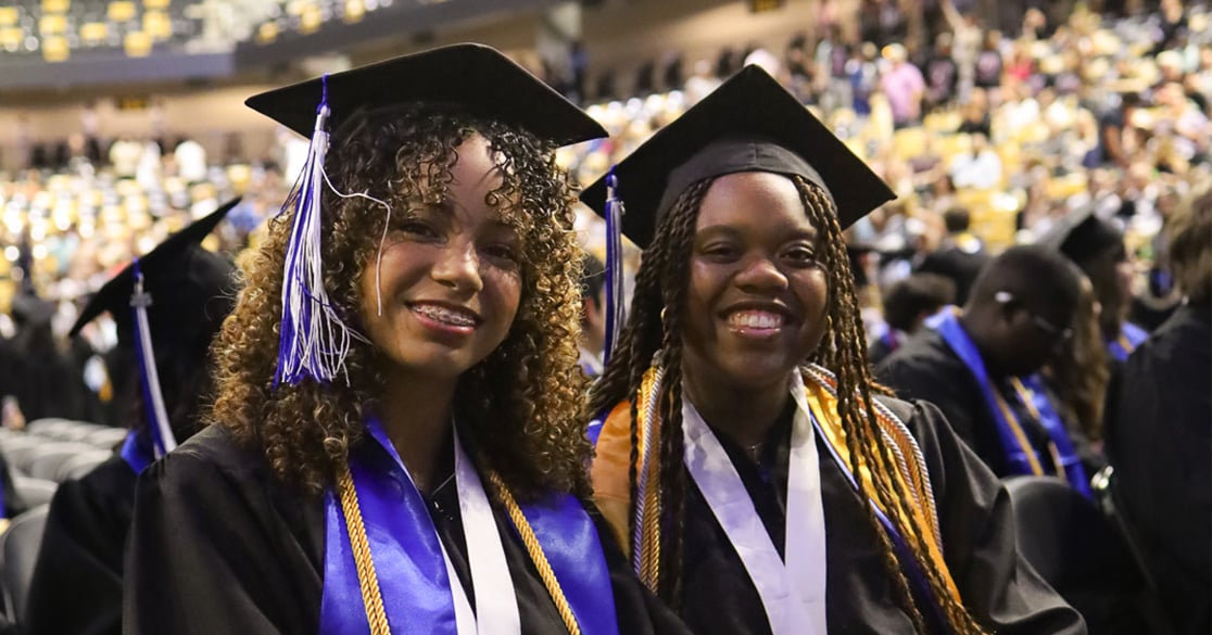 Two Florida Virtual High School seniors in their caps and gowns smile at the camera during their graduation ceremony.