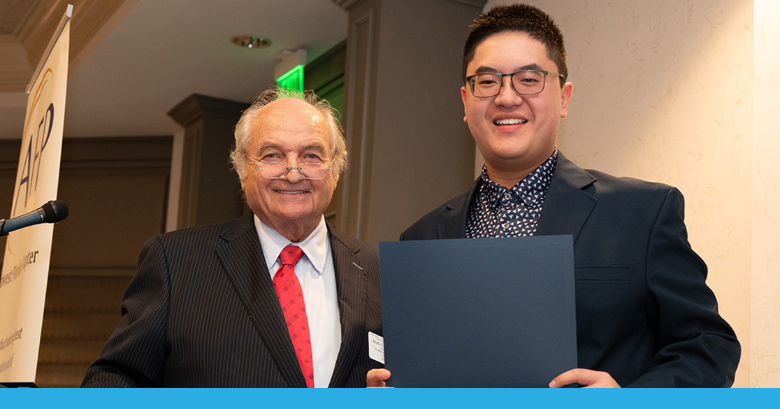 Alvin Luu stands indoors holding his certificate for his the Youth in Philanthropy Award.