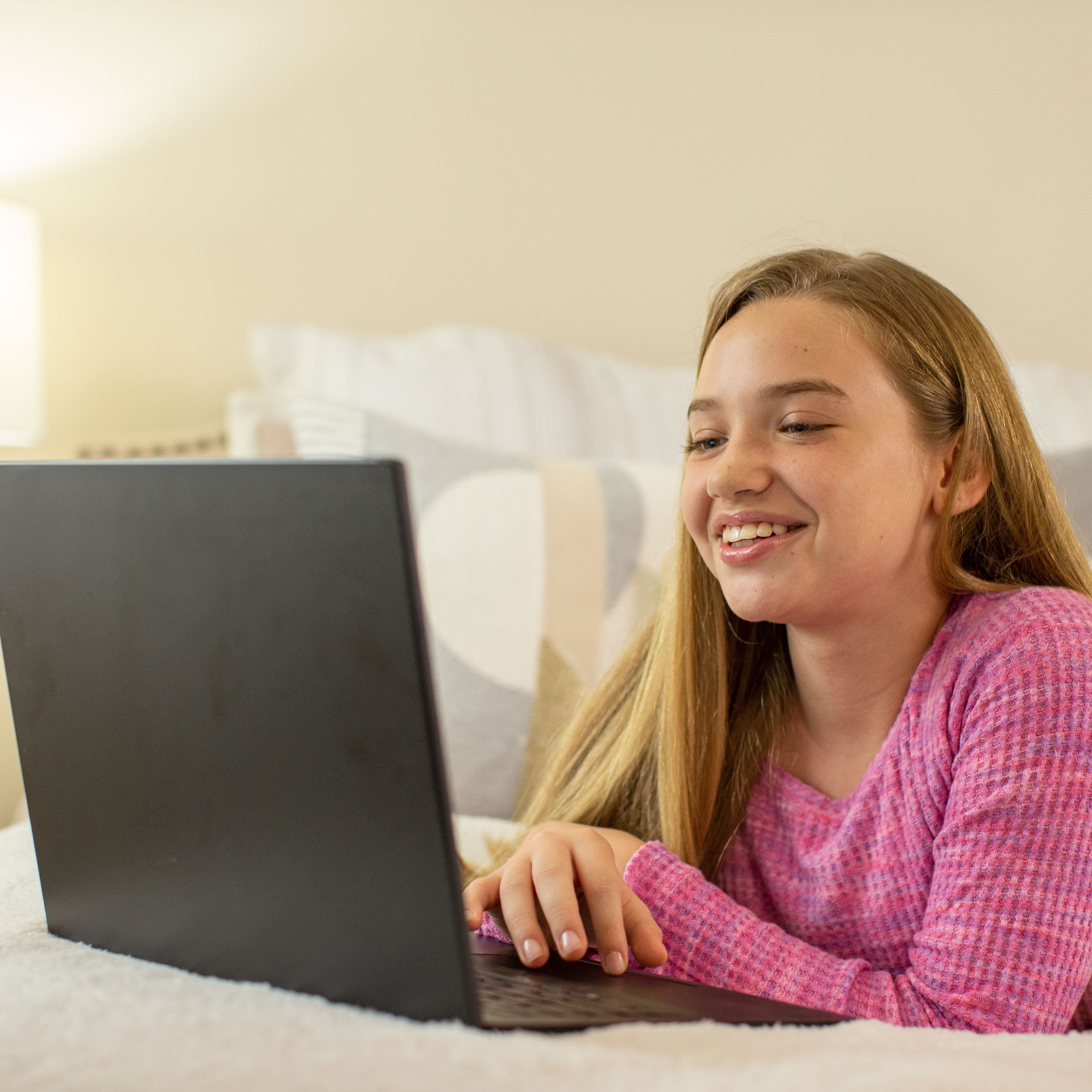 Teenage girl laying on bed looking at her laptop