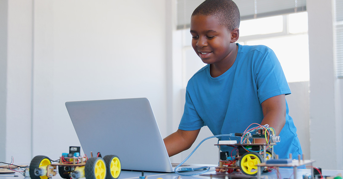 A young student stands in front of a laptop working on his Florida Virtual School course for coding with robots on the table next to him.