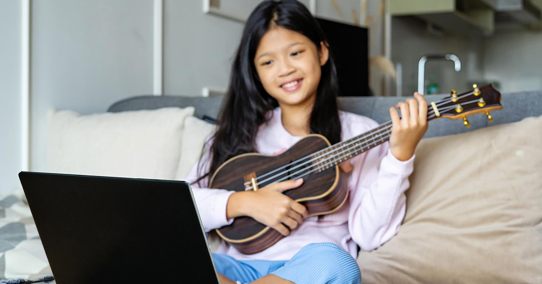 A student uses a small string instrument as part of an online music activity