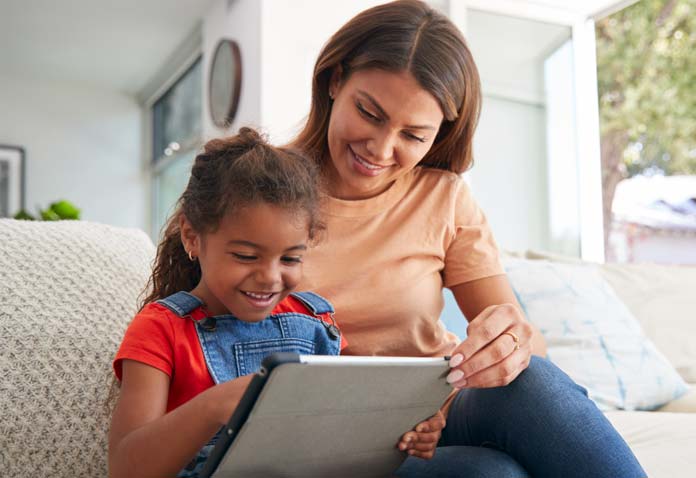 A mother, acting as a Learning Coach, helps her young daughter complete her FLVS elementary online school work on a tablet.