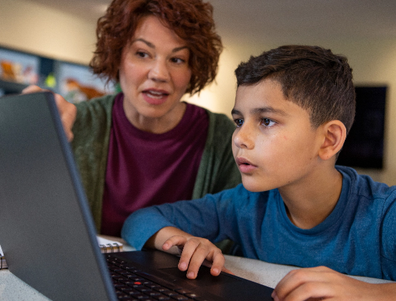 A mother or Learning Coach provides one-on-one guidance to an elementary student focused on his FLVS online course on a laptop.