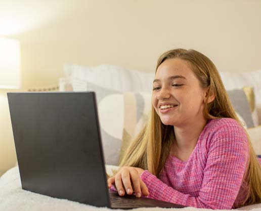 Student using a laptop while sitting on a bed.