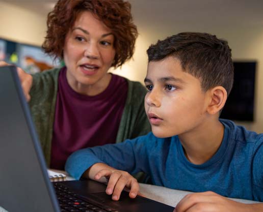 Person helping a child use a laptop computer.