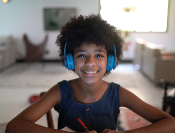 Young female FLVS Full Time Public School student smiling while participating in online learning with blue headphones on.