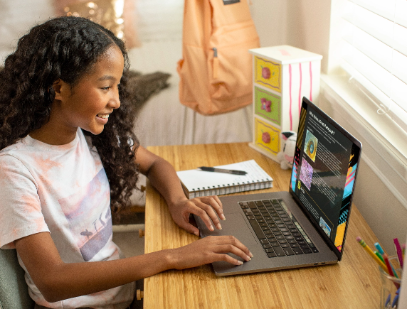 Smiling middle school student working independently on her FLVS virtual course curriculum using a laptop at her home desk.