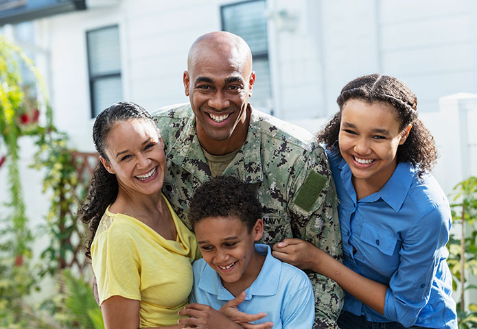 Service member in uniform standing outdoors with three children, gathered together for a family photo