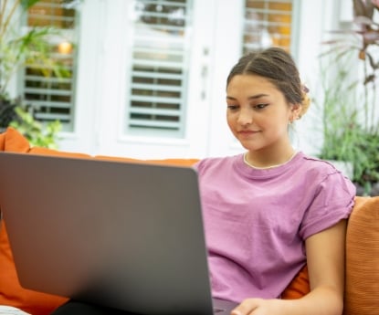 Teenage girl comfortably studying on a laptop outdoors on a patio sofa. This image highlights the flexibility and anytime, anywhere access of the FLVS Flex individual courses.